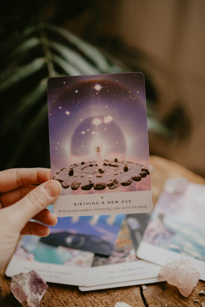 Tarot card held in hand, surrounded by crystals and plants, indoors.